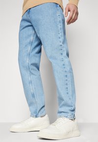 Vaaleansiniset farkut rentolla istuvuudella, suorat lahkeet ja haalistunut viimeistely, yhdistettynä valkoisiin tennareihin.