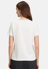 Weißes Baumwoll-T-Shirt mit rundem Ausschnitt und kurzen Ärmeln, das eine glatte Textur und ein minimalistisches Design zeigt. Der Saum endet auf Hüfthöhe.
