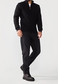 Czarny sweter z zamkiem na szyi, wykonany z teksturowanego splotu, w połączeniu z ciemnoniebieskimi dżinsami i czarnymi sznurowanymi butami. Prosty i funkcjonalny design.