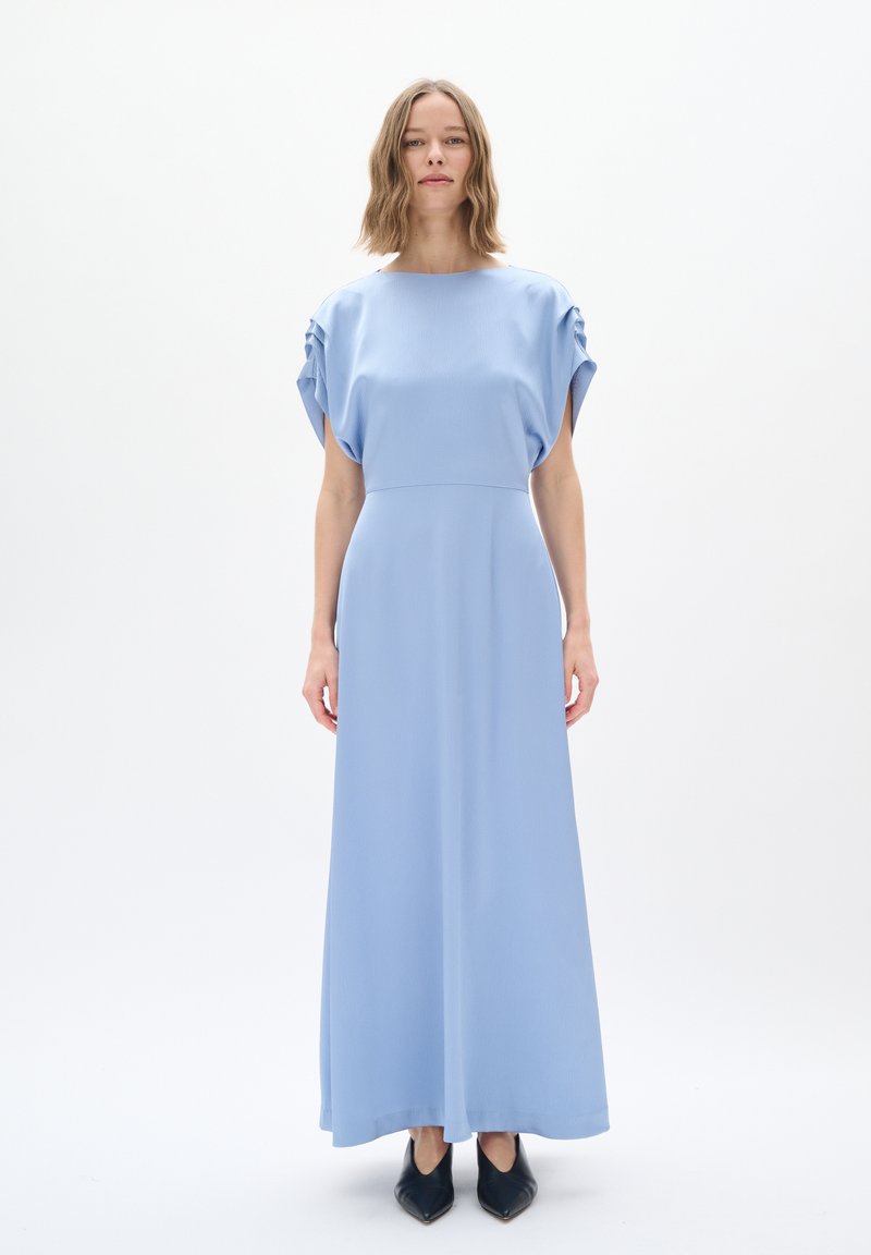 Abito maxi azzurro chiaro con una vestibilità rilassata, dotato di maniche a sbuffo corte e una texture liscia. Abbinato a scarpe a punta blu scuro.