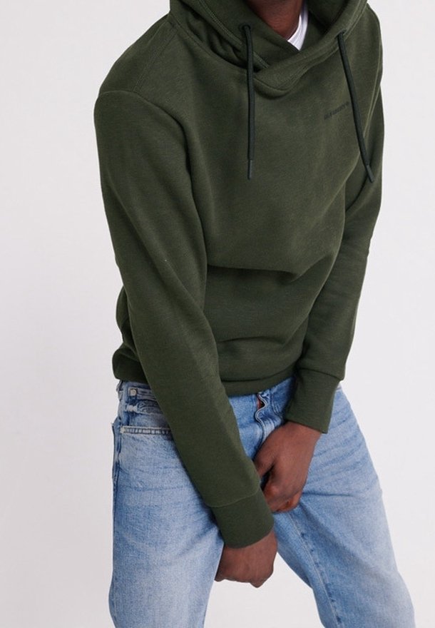 Felpa verde oliva con collo alto, lacci e vestibilità comoda, abbinata a jeans azzurri chiari. Tessuto morbido con un design minimalista.