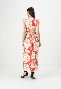 Sleeveless maxi dress with a fitted bodice and flared skirt, featuring a red background and large cream floral patterns. Black high-heeled shoes.