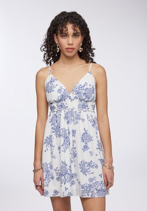 Abito floreale bianco con motivi botanici blu, scollatura a V, spalline regolabili e vita arricciata, che crea una silhouette a campana.