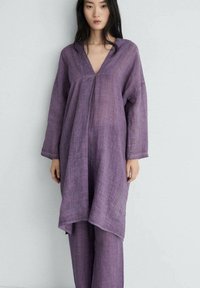 Violet linnen tunika med V-urringning och långärmar, parat med matchande vida byxor. Tyget har en texturerad och andningsbar look.
