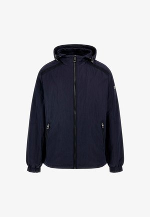 Chaqueta navy azul con cremallera y capucha, hecha de un tejido ligero arrugado. Cuenta con puños elásticos y dos bolsillos frontales con cremallera.