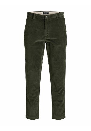 Homme portant un pull zippé noir en maille torsadée, une chemise blanche à rayures, un pantalon en velours côtelé vert, tenant une veste beige et des chaussures marron sur fond blanc.