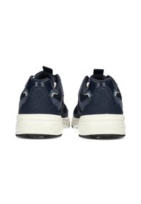 Un paio di sneakers sportive blu navy con suole bianche viste da dietro su uno sfondo bianco.