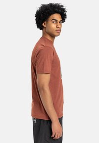 Short-sleeve rust-colored t-shirt in a soft, textured fabric with a crew neck. Features a graphic design on the front.