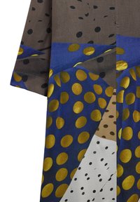 Brązowy i niebieski materiał z dużymi złotymi, czarnymi i białymi kropkami w abstrakcyjnym geometrycznym wzorze na rękawie odzieży.