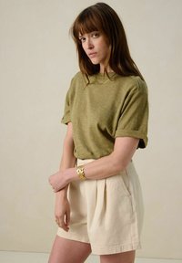 Haut olive à manches courtes avec un col rond, associé à un short taille haute beige clair et un bracelet floral en or.