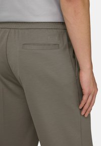 Pantalon de sport vert foncé avec une texture de tissu lisse, doté d'une poche arrière et d'un logo discret en relief sur la ceinture.