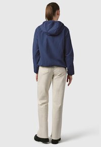 Tamsiai mėlyna gobtuvu užsegama striukė laisvo kirpimo, derinama su kreminės spalvos kelnėmis. Kelnės turi struktūruotą dizainą ir šiek tiek išplatėja apačioje.