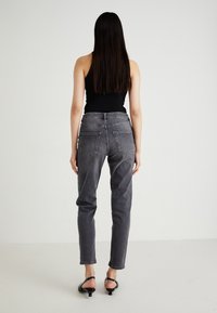 Pielāgotas pelēkas džinsa bikses ar piecu kabatu dizainu, taisnu kāju un vieglu nolietojumu. Modelis valkā melnu tank top un papēžsandales.