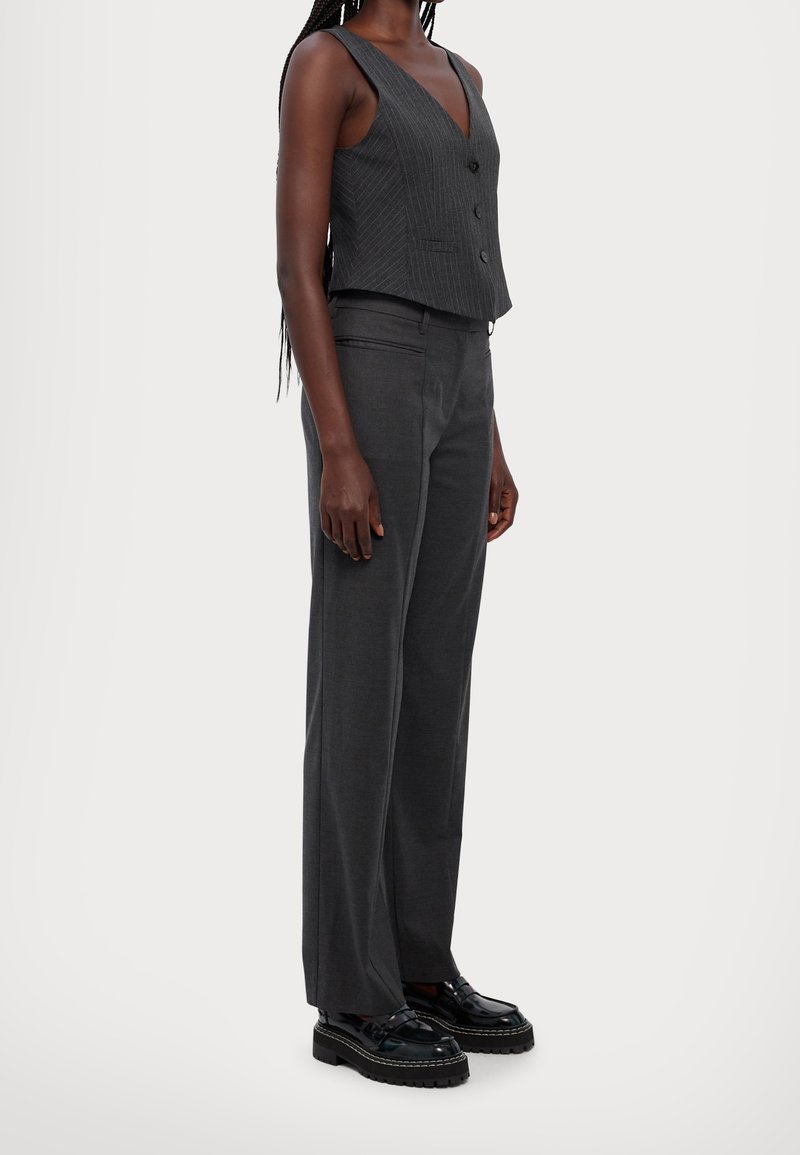 Grå rutiga västar med v-ringning, knappstängning, i kombination med matchande smala byxor. Avslutat med glänsande svarta skor.