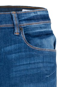 Jeans de denim azul oscuro con costuras naranjas, un bolsillo frontal, cierre de botón y acabado de tela texturizada. Presenta una cinturilla con pasadores para el cinturón.
