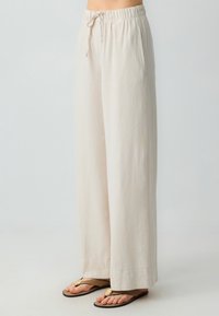 Lichtbeige wijde broek met een elastische tailleband en koord, voorzien van zijzakken en een zachte, gestructureerde stof.