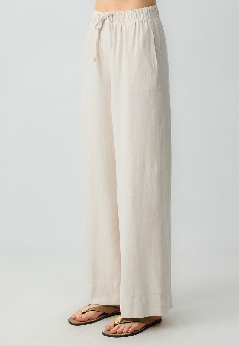 Lichtbeige wijde broek met een elastische tailleband en koord, voorzien van zijzakken en een zachte, gestructureerde stof.