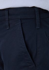 Pantalones de algodón azul marino con una textura suave, que presentan bolsillos frontales y pasadores para cinturón, mostrando costuras detalladas y un diseño a medida.
