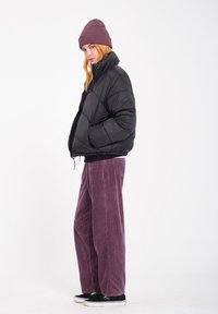 Giacca a vento nera, con zip frontale e polsini a coste. Abbinata a pantaloni in corduroy viola a gamba larga e un berretto a coste. Sneakers nere completano il look.