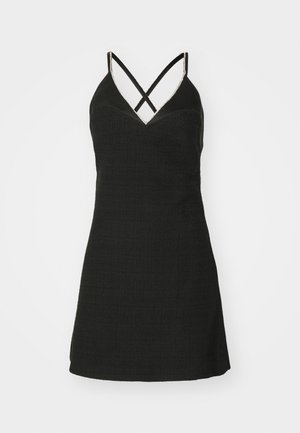 Sort kjole med tekstureret stof, V-udskæring og krydsede stropper. Den har en tætsiddende overdel og en siddende nederdel.