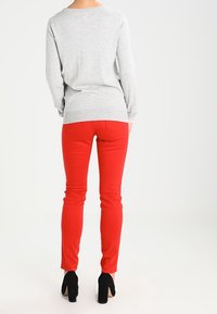 Maglione grigio a maniche lunghe con scollatura rotonda abbinato a pantaloni rossi aderenti. Stivali neri alla caviglia completano l'outfit.