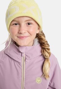 Lila vízálló dzseki sárga cipzárral és logóval, puha sárga kötött sapkával párosítva, fehér mintákkal.