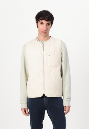 Beige quilted vest with a round neckline, front zip closure, and a chest pocket. Worn over a light green long-sleeve shirt.