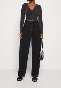 Svart, stretchig långärmad topp med djup V-ringning; högmidjade svarta vida jeans; kraftiga svarta sandaletter; liten svart handväska.