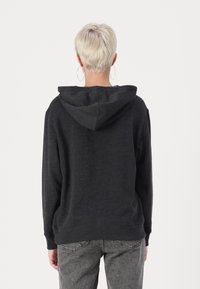 Hanorac negru cu glugă, cu o textură moale și croială lejeră. Are un buzunar clasic tip kangaroo și manșete ribbate, asortat cu pantaloni gri.