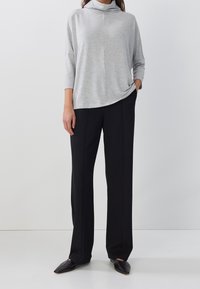 Hellgraues langärmliges Oberteil mit Kragen, kombiniert mit schwarzen geraden Hosen und schwarzen spitz zulaufenden Ballerinas auf einem einfarbigen Hintergrund.