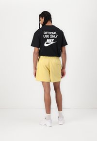 Μαύρο t-shirt με λευκό κείμενο "ΜΟΝΑΔΙΚΗ ΧΡΗΣΗ" και λογότυπο Nike, συνδυασμένο με κίτρινες βερμούδες, ελαστική μέση και πίσω τσέπη. Λευκά αθλητικά πα�πούτσια.