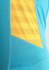 Světle modré sportovní tričko s designem žlutého perforovaného pruhu, jemnou strukturou a kontrastním stehem na boku.