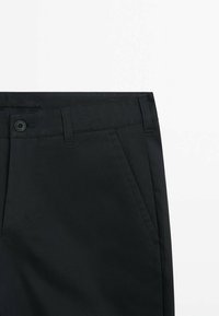 Black trousers made of smooth fabric feature a straight cut, front pockets, and a button closure. Simple design with no visible patterns.