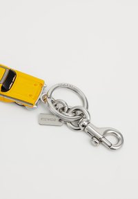 Yellow taxi cab keychain made of plastic, featuring silver stainless steel hardware. Includes a tag embossed with "COACH."