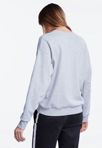 Sudadera gris claro con un corte relajado, puños y dobladillo acanalados, y cuello redondo. Vista desde la parte posterior, mostrando una textura suave y costuras.