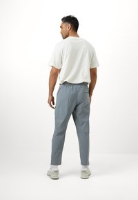 Gaiši pelēkas elastīgas jostas bikses ar sānu kabatām un sašaurinātiem kāju galiem, apvienotas ar brīva piegriezuma baltu T-kreklu ar apaļu kakla izgriezumu.