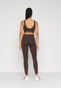 Brun sports-bh og højtaljede leggings lavet af fleksibelt materiale. Bh'en har et bredt stropdesign; leggingsene har en glat tekstur og en tætsiddende form.