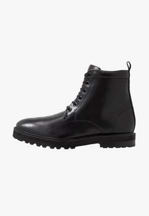 Bottine en cuir noir avec lacets à l'avant, semelle texturée et languette à l'arrière, conçue pour la durabilité et le style.