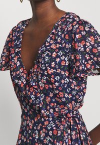 Kwiatowa sukienka z falbaniastymi rękawami, na głębokim granatowym tle, z małymi różowymi, białymi i zielonymi kwiatami. Lekki materiał, talia wcięta paskiem.