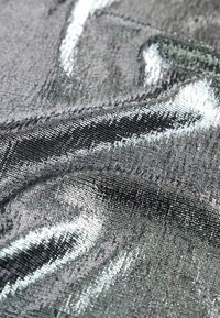 Textúrovaná tkanina s metalicky strieborným a čiernym vzorom, s hladkými, lesklými vláknami vytvárajúcimi vlnité vzory na povrchu.