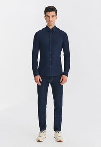 Granatowa koszula na guziki o dopasowanym kroju, z długimi rękawami i kołnierzykiem, zestawiona z ciemnymi jeansami i białymi sneakersami. Gładka faktura tkaniny.