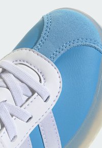 Baskets bleues avec une tige en cuir lisse et en daim, lacets blancs et semelle texturée. Des détails de couture remarquables mettent en valeur le design.