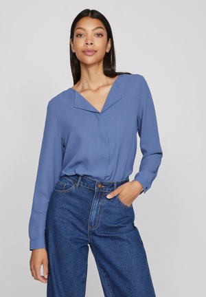 Light blue long-sleeve blouse with a v-neck design, made of soft fabric. Paired with high-waisted dark blue jeans featuring front pockets.