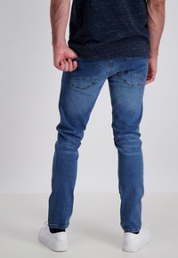 Jeans denim w średnim niebieskim pralce o slim fit, z tylnymi kieszeniami i gładką fakturą, zestawione z białymi trampkami.