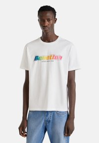 Bílý bavlněný tričko s barevným logem "Benetton", kulatým výstřihem, krátkým rukávem a volným střihem.