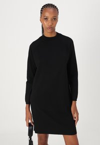 Melnas garās piedurknes kleitas, kas izgatavota no mīksta auduma, ar apļa kakla izgriezumu un brīvu piegriezumu, beidzas virs ceļgaliem ar ribotu apdari.