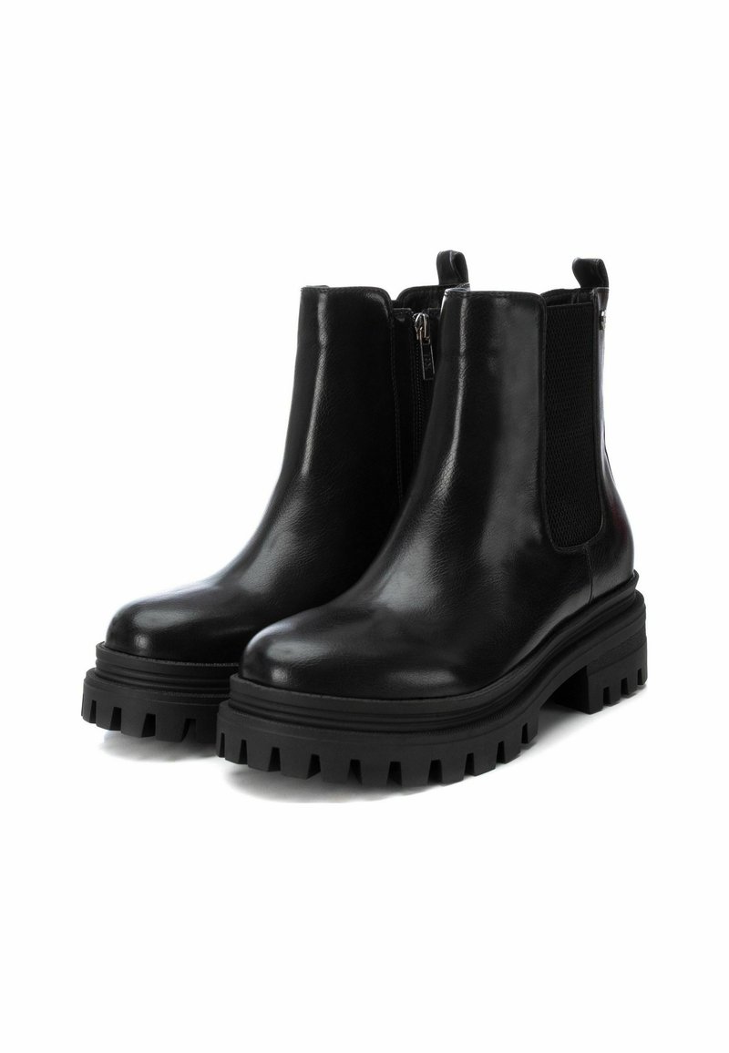 Bottines en cuir noir avec panneaux élastiques sur les côtés, semelle texturée noire, design chunky et fermeture éclair. Fini lisse avec une apparence brillante.