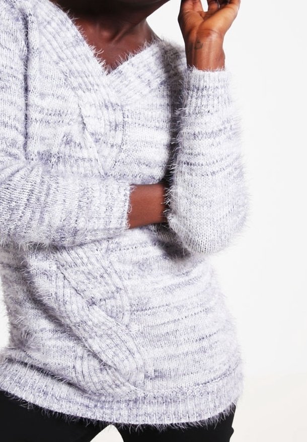 Ljusgrå stickad tröja med V-ringning, utrustad med ett flätmönster och texturerad, lurvig garn. Långa ärmar med ribbade manschetter.