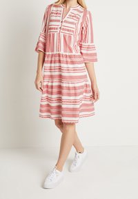 Rot-weißer gemusterter Kleid mit Dreiviertelärmeln, tailliertem Bund und gerafftem Rock, kombiniert mit weißen Sneakern.