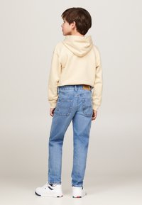 Felpa beige con cappuccio e tasca a marsupio, abbinata a jeans di denim azzurro chiaro con tasche posteriori. Sneakers bianche con dettagli neri.